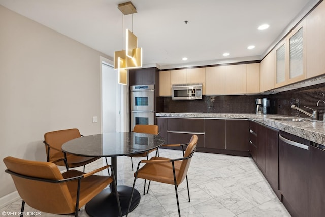 kitchen with appliances with stainless steel finishes, backsplash, dark brown cabinets, sink, and decorative light fixtures