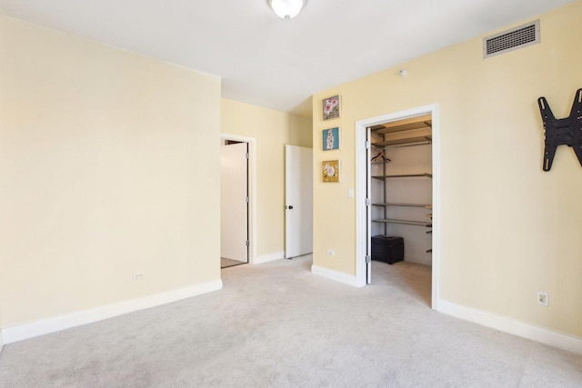 unfurnished bedroom with a walk in closet, a closet, and light colored carpet