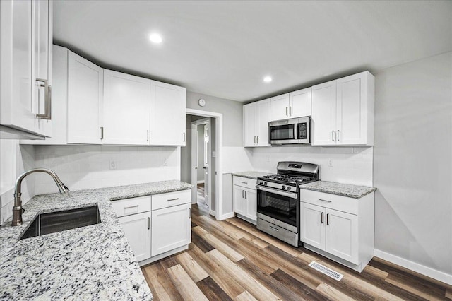 kitchen featuring white cabinetry, sink, light stone countertops, stainless steel appliances, and hardwood / wood-style floors