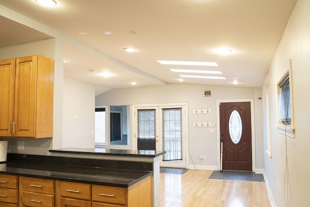 kitchen with vaulted ceiling with skylight, light hardwood / wood-style floors, and french doors