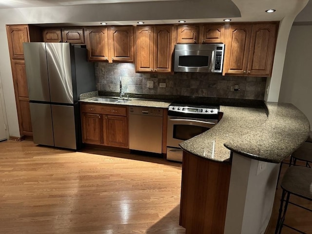 kitchen featuring light stone countertops, sink, stainless steel appliances, backsplash, and light wood-type flooring