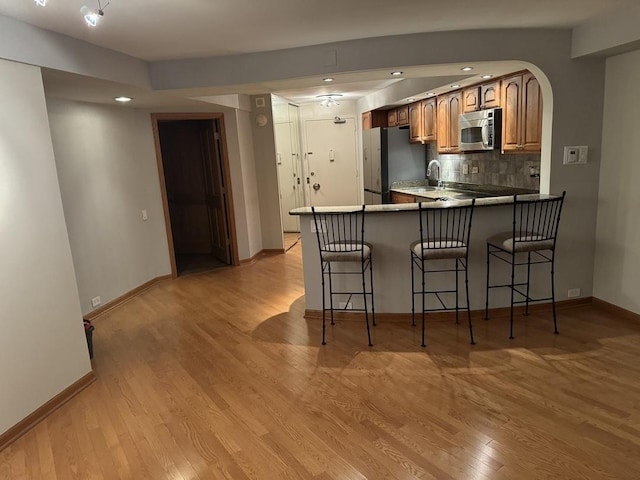 kitchen featuring stainless steel appliances, a kitchen breakfast bar, tasteful backsplash, kitchen peninsula, and light wood-type flooring