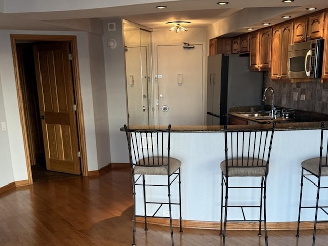 kitchen with stainless steel appliances, dark hardwood / wood-style floors, a kitchen breakfast bar, decorative backsplash, and kitchen peninsula