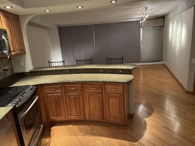 kitchen with light stone counters, light hardwood / wood-style flooring, an AC wall unit, appliances with stainless steel finishes, and kitchen peninsula