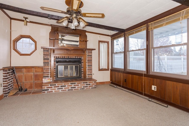 unfurnished living room featuring a fireplace, ceiling fan, beamed ceiling, carpet floors, and wood walls