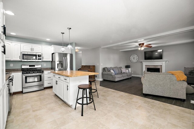 kitchen featuring pendant lighting, white cabinets, a kitchen island, butcher block counters, and stainless steel appliances