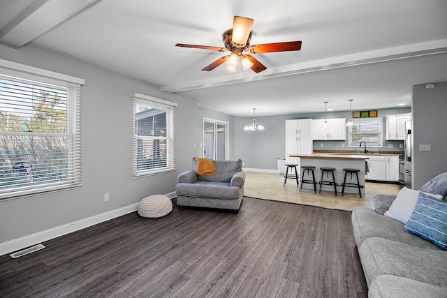 living room with beamed ceiling, ceiling fan with notable chandelier, hardwood / wood-style flooring, and sink