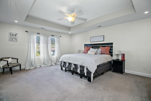 carpeted bedroom with ceiling fan and a raised ceiling