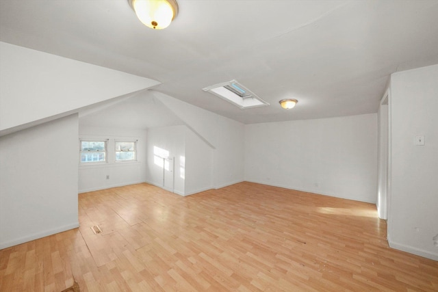 bonus room with vaulted ceiling with skylight and light wood-type flooring