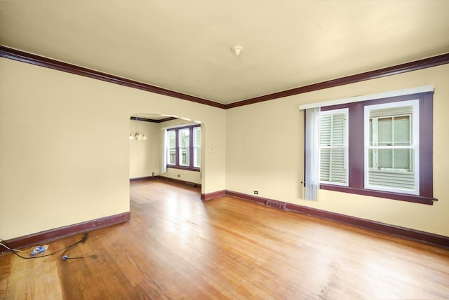 empty room featuring hardwood / wood-style floors, ornamental molding, and a chandelier