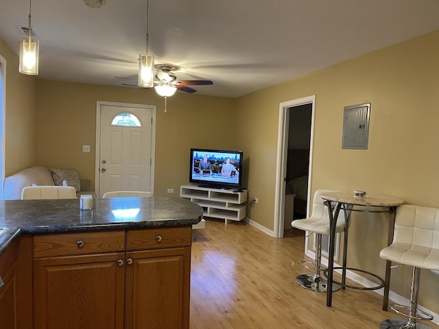 kitchen featuring ceiling fan, a kitchen breakfast bar, electric panel, pendant lighting, and light wood-type flooring