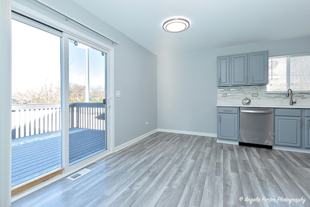 kitchen with stainless steel dishwasher, plenty of natural light, backsplash, and light hardwood / wood-style flooring