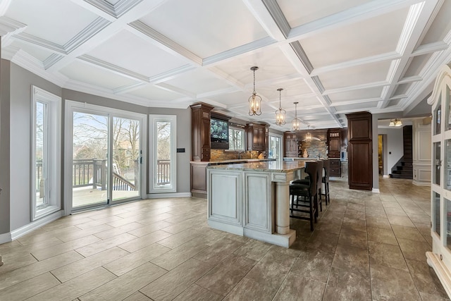 kitchen with a kitchen breakfast bar, backsplash, coffered ceiling, a kitchen island, and hanging light fixtures