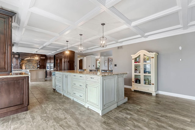 kitchen featuring stainless steel oven, coffered ceiling, light stone counters, pendant lighting, and a spacious island