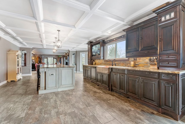 kitchen featuring dark brown cabinetry, a chandelier, decorative light fixtures, decorative backsplash, and a kitchen island