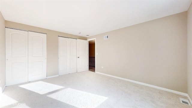 unfurnished bedroom featuring light carpet and multiple closets