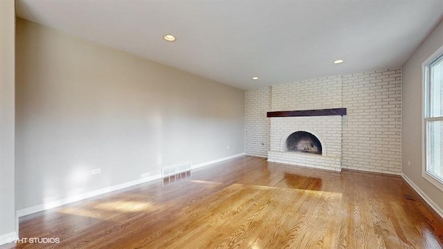 unfurnished living room featuring wood-type flooring, brick wall, and a brick fireplace