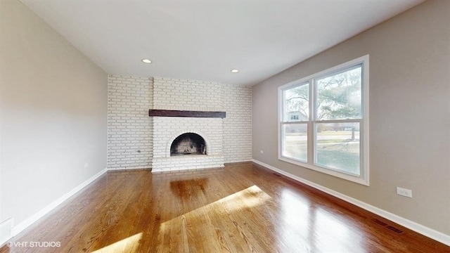 unfurnished living room featuring hardwood / wood-style flooring and a brick fireplace