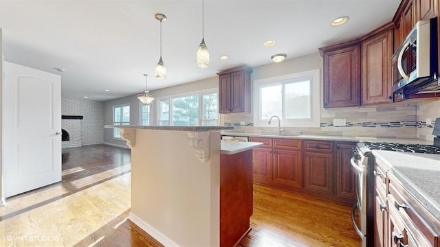 kitchen with pendant lighting, a kitchen bar, light hardwood / wood-style flooring, light stone counters, and stainless steel appliances