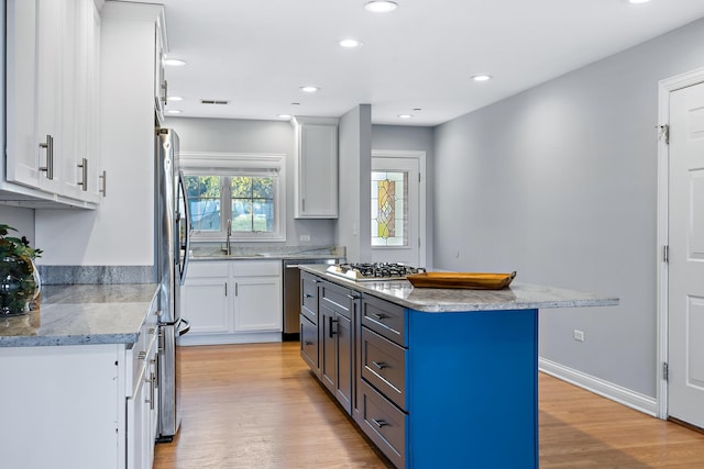 kitchen with appliances with stainless steel finishes, white cabinets, light wood-type flooring, and a kitchen island