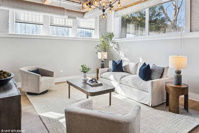 living area with light wood-style floors, baseboards, and an inviting chandelier