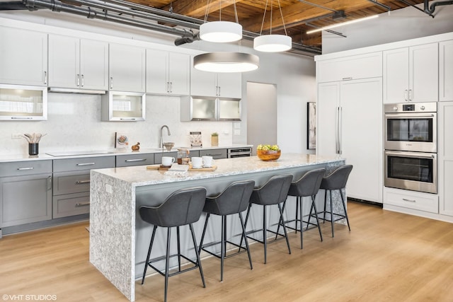 kitchen with a kitchen island, paneled built in refrigerator, gray cabinetry, double oven, and pendant lighting