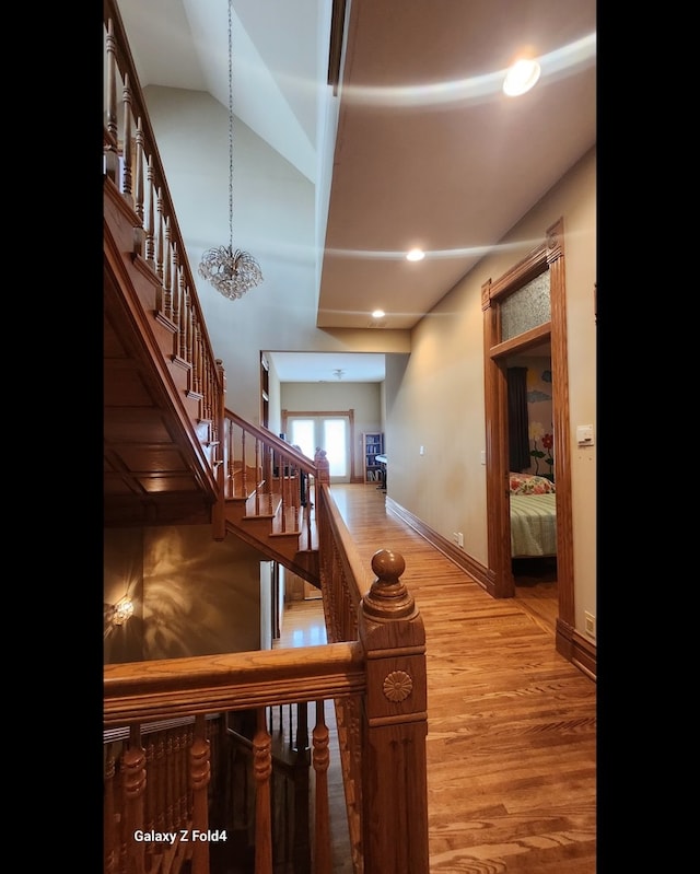 stairway with lofted ceiling, wood-type flooring, and an inviting chandelier