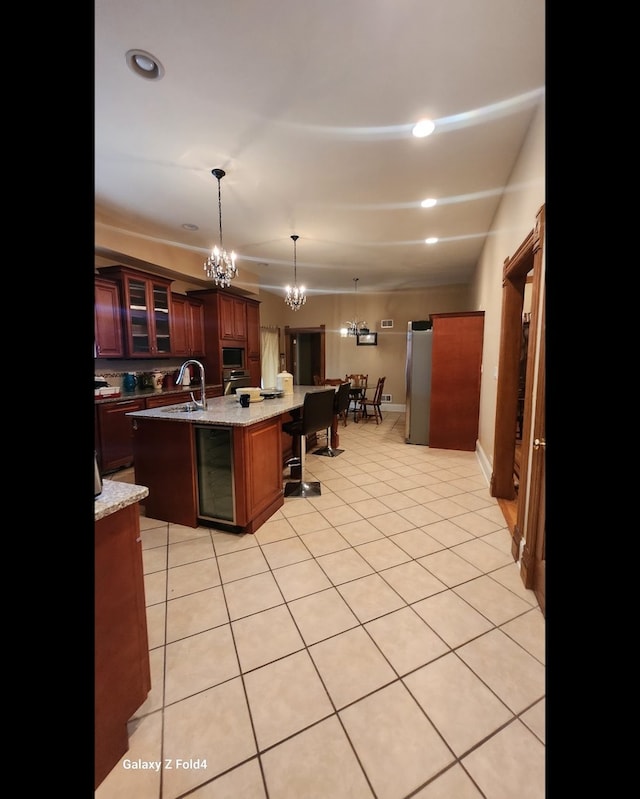 kitchen with stainless steel appliances, hanging light fixtures, wine cooler, a kitchen island with sink, and light tile patterned floors