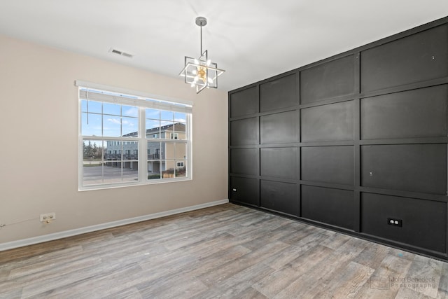 spare room with light hardwood / wood-style floors and a notable chandelier