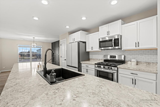 kitchen featuring white cabinets, hanging light fixtures, sink, appliances with stainless steel finishes, and wood-type flooring