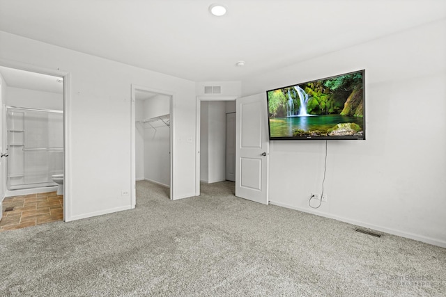 unfurnished bedroom featuring carpet flooring, a walk in closet, ensuite bathroom, and a closet