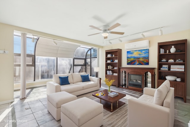 living area with a glass covered fireplace, a wall mounted air conditioner, ceiling fan, and rail lighting