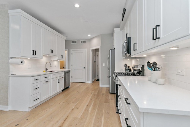 kitchen featuring backsplash, white cabinets, sink, light hardwood / wood-style flooring, and stainless steel appliances