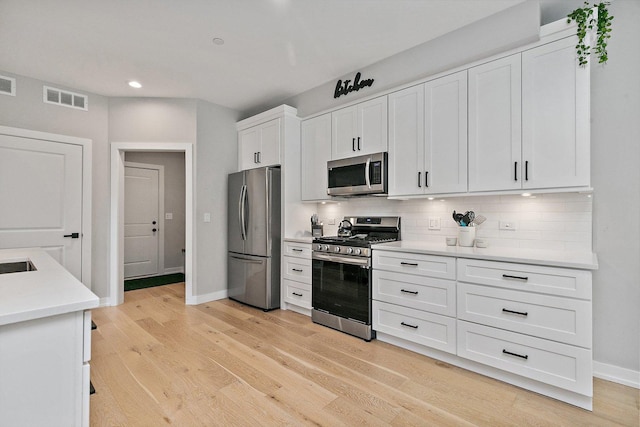 kitchen with decorative backsplash, white cabinets, stainless steel appliances, and light hardwood / wood-style floors