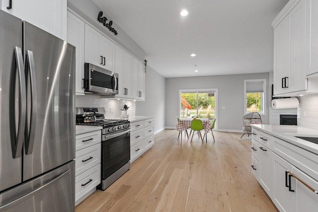 kitchen with backsplash, light hardwood / wood-style floors, white cabinetry, and stainless steel appliances