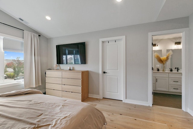 bedroom with light wood-type flooring, connected bathroom, and vaulted ceiling