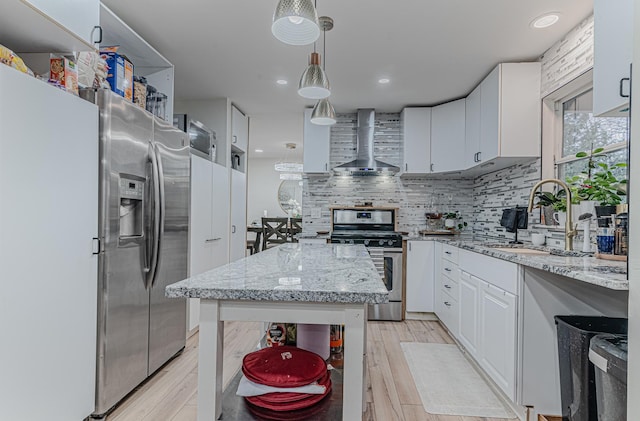 kitchen with white cabinets, hanging light fixtures, light hardwood / wood-style flooring, wall chimney exhaust hood, and appliances with stainless steel finishes