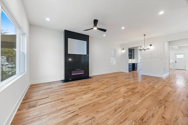 unfurnished living room featuring a wealth of natural light, ceiling fan with notable chandelier, and light wood-type flooring