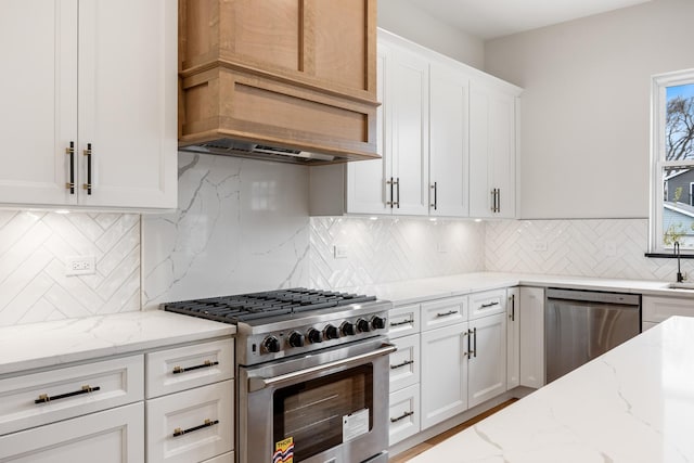 kitchen with light stone countertops, tasteful backsplash, appliances with stainless steel finishes, white cabinets, and custom exhaust hood