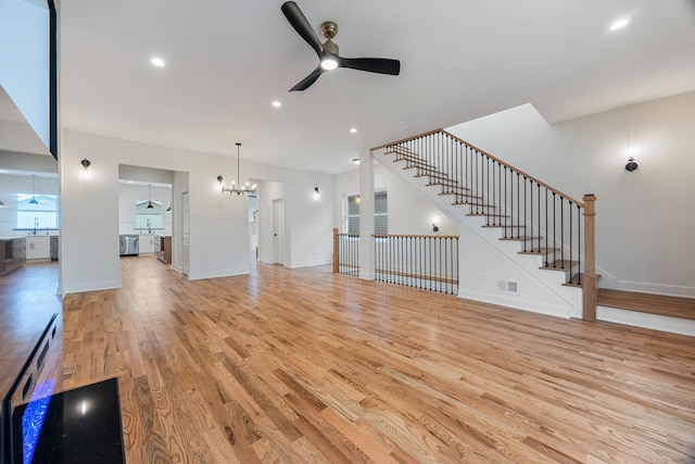 unfurnished living room with ceiling fan with notable chandelier and light hardwood / wood-style flooring