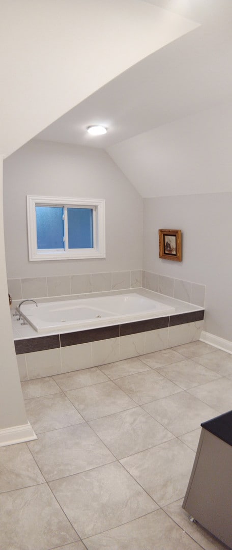 bathroom featuring vaulted ceiling and tiled tub