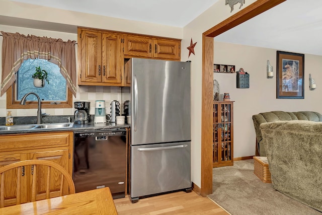 kitchen featuring sink, light hardwood / wood-style flooring, decorative backsplash, stainless steel fridge, and black dishwasher