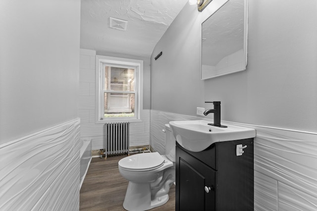 bathroom with radiator, vanity, tile walls, hardwood / wood-style floors, and toilet