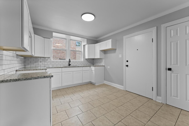 kitchen featuring tasteful backsplash, ornamental molding, sink, dark stone countertops, and white cabinets