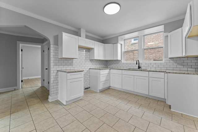 kitchen with white cabinets, light stone countertops, crown molding, and sink