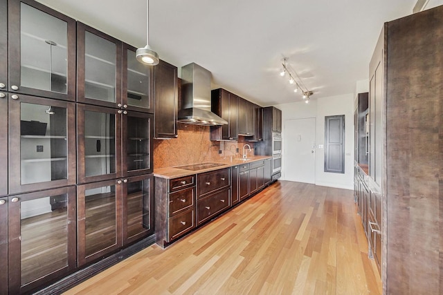 kitchen featuring light wood-type flooring, tasteful backsplash, sink, wall chimney range hood, and decorative light fixtures