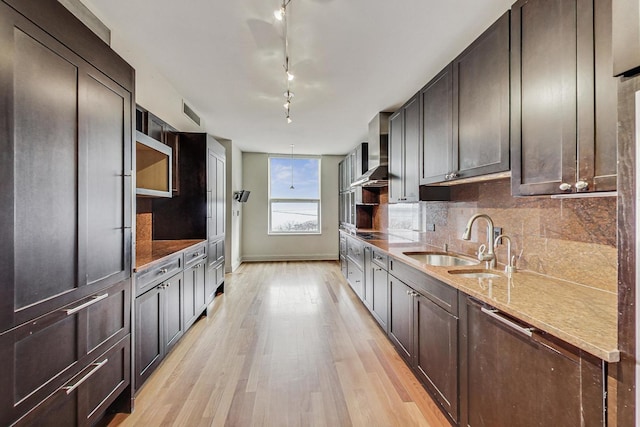 kitchen with sink, wall chimney range hood, light stone counters, light hardwood / wood-style floors, and track lighting