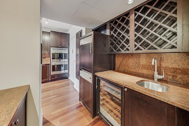 kitchen featuring sink, wine cooler, light wood-type flooring, double oven, and tasteful backsplash