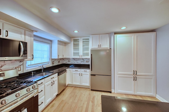 kitchen with white cabinets, appliances with stainless steel finishes, backsplash, and light hardwood / wood-style floors