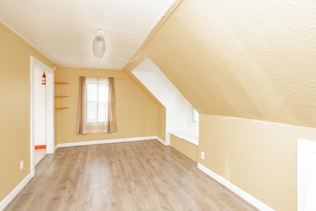 additional living space featuring lofted ceiling, light wood-type flooring, and a textured ceiling